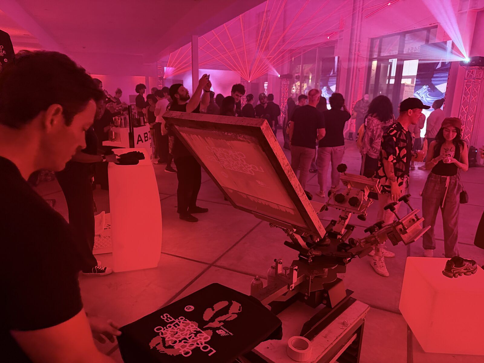 Operator pulling a print at a pink-lit indoor brand party while guests mingle